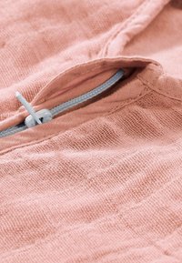 Light pink textile featuring a textured surface, with a close-up view of a zippered opening and a contrasting grey zipper pull.