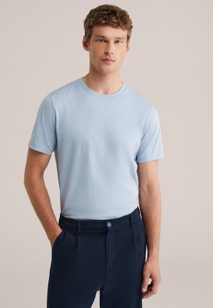 Tricou bleu deschis cu mâneci scurte și decolteu rotund, confecționat dintr-un material neted. Asortat cu pantaloni bleumarin închis, cu nasture albastru vizibil.