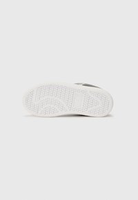Semelle extérieure en caoutchouc blanc avec un motif de texture et un design incurvé. Présente le logo de la marque "EA3" embouti sur le côté.