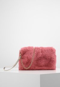 Pochette en fausse fourrure rose de forme rectangulaire. Dotée d'une bandoulière chaîne dorée et d'une texture lisse, contrastant avec l'extérieur doux.