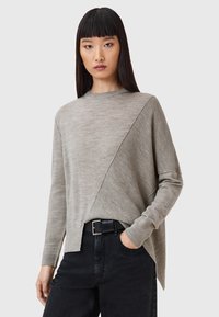 Maglione grigio chiaro con una texture mista, caratterizzato da un design a coste diagonali, polsini a coste e una vestibilità rilassata, abbinato a jeans neri.