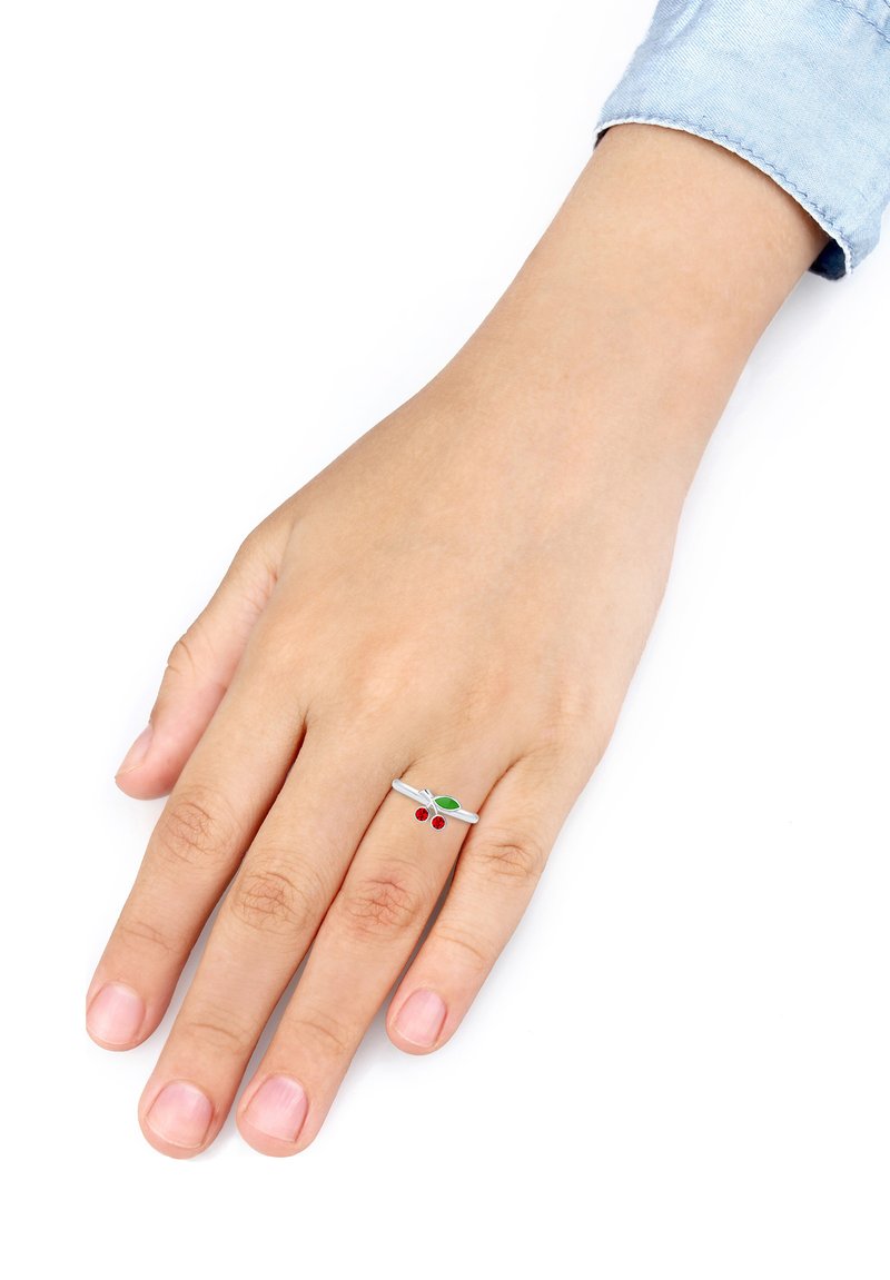 Anello in argento con una band liscia che presenta due ciliegie di gemma rossa e un accento di foglia verde. Appoggiato su una mano umana con finitura naturale delle unghie.