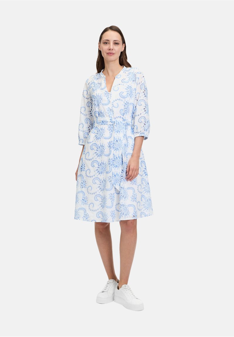 Abito stampato blu chiaro e bianco con scollatura a V, maniche a tre quarti, vita aderente e gonna a campana, abbinato a sneakers bianche.