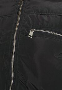 Black padded jacket featuring a prominent silver zipper, textured fabric, and a zippered chest pocket for added functionality.