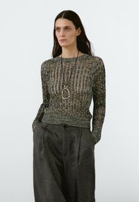 Strickpullover in dunklen Tönen, mit einem offenen Strickdesign, langen Ärmeln und einem engen Saum. Kombiniert mit hochtaillierten, lockeren dunklen Hosen.