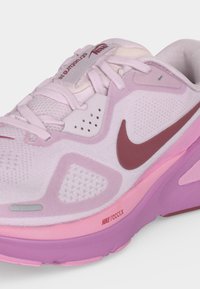 Ανοιχτό ροζ αθλητικό παπούτσι Nike με σκούρο ροζ σήμα, πλεκτό επάνω μέρος, λευκά κορδόνια και μοβ-ροζ σόλα με την ετικέτα "Nike React".