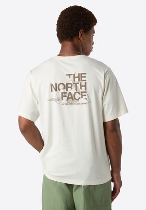 Man wearing cream t-shirt with "THE NORTH FACE" and mountain graphic on back, paired with green shorts, facing away from camera.