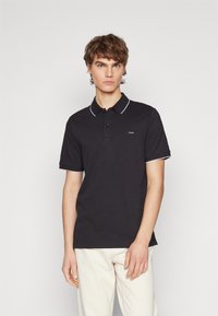 Black polo shirt made of cotton, featuring a classic collar with white piping and a small logo on the left chest. Short sleeves.