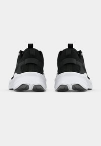 Paire de baskets de sport noires avec semelles blanches épaisses, vues de dos sur un fond gris uni.