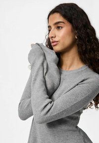 Pull gris à manches longues à côtes avec un col rond. Texture douce, coupe ajustée et manches allongées pouvant être tirées sur les mains.