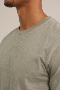 Pelēks kokvilnas T-krekls ar apaļu kakla izgriezumu, ar gludu tekstūru un īsām piedurknēm, parādīts no sānu skata.