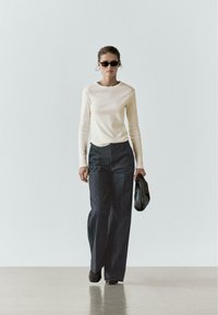 Langærmet cremefarvet top kombineret med højttaljede mørke denimbukser med vide ben. Sorte solbriller og en sort clutch fuldender looket.