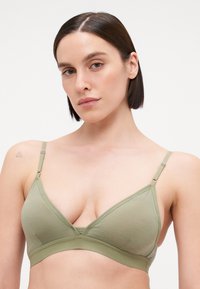 Sutiã verde oliva claro com copas triangulares, alças ajustáveis e uma textura suave. Apresenta um design sem costuras e mínimos accents de metal.