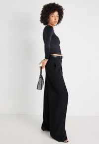 Melna gara piedurkne blūze ar teksturētu rakstu, apvienota ar augsto jostasvietu platām biksēm. Aksesuāri - mazs, spīdīgs roku somiņš.