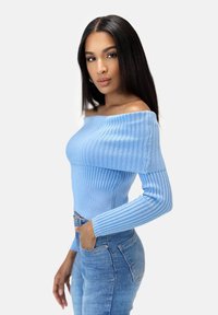 Hellblaues schulterfreies Sweatshirt mit geripptem Muster und langen Ärmeln, kombiniert mit enganliegenden blauen Jeans. Glatter Stoff, figurschnittbetonendes Design.