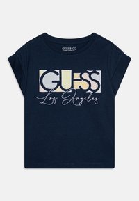 Camiseta de manga corta azul marino hecha de algodón orgánico, con un gran logo multicolor de "GUESS" y el texto en cursiva "Los Ángeles" en el centro.
