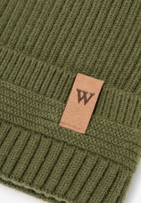 Berretto verde lavorato a maglia con trama coste e una toppa in pelle color cuoio con monogramma marrone. Materiale morbido e caldo.