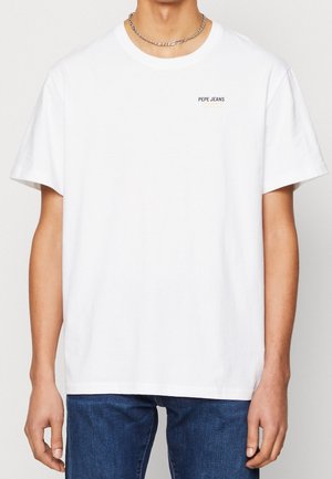 Mann trägt ein weißes Pepe Jeans T-Shirt mit kurzen Ärmeln und eine silberne Gliederkette, kombiniert mit blauen Jeans.