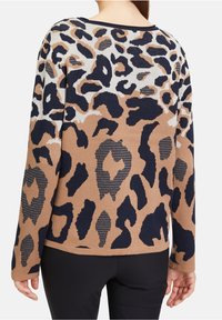 Pull à imprimé léopard avec un mélange de couleurs beige, noir et blanc, présentant un design en maille texturée et une coupe décontractée, manches longues.