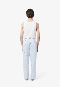 Witte tanktop met blauwe gestreepte pyjamabroek met groene logo-accenten. De tailleband heeft een gebrandmerk elastische band. Effen achtergrond.