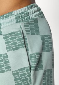 Calças de treino verdes com um padrão de logótipos Puma por toda a parte, cintura elástica e material suave em mistura de algodão.