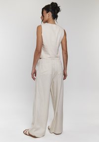 Beige linne ärmlös topp som matchas med löst sittande beige byxor med två bakfickor. Slät textur och avslappnad silhuett.