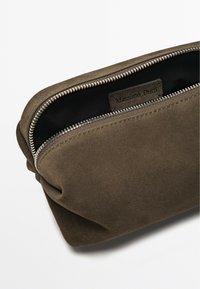 Hnědá suedená kosmetická taška se zipovým uzávěrem, uvnitř s etikou. Měkká textura a jednoduchý design bez viditelných vzorů.