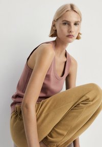 Roze mouwloze tanktop, gecombineerd met zachte, goudkleurige jogpants die een gladde textuur en een ontspannen pasvorm laten zien.