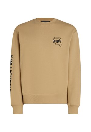 Felpa beige realizzata in un tessuto morbido, con una grafica a cartone animato nera sul petto e il testo "KARL LAGERFELD" sulla manica sinistra.