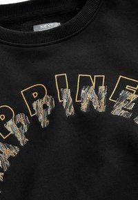 Sweat-shirt noir avec col côtelé comportant des lettres brodées en or formant le mot « HAPPINESS » et des motifs à imprimé animal.
