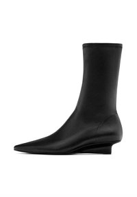 Stivale nero alla caviglia con una silhouette elegante e aderente. Realizzato in materiale liscio, presenta una punta affilata e un tacco a trapezio basso.