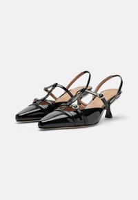 Scarpe slingback in pelle verniciata nera con punta affusolata, cinturini incrociati, piccoli dettagli circolari e tacco a cono basso.