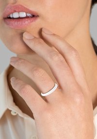 Bela, gladka prstana nositi na prstu, z minimalističnim dizajnom. Roka se rahlo dotika brade na nevtralni podlagi.