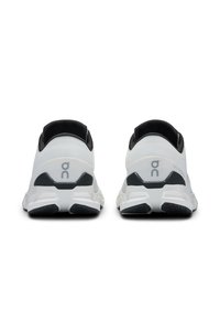 Des chaussures de sport blanches avec des accents noirs, présentant un empeigne en mesh texturé, un talon rembourré et un design de semelle distinctif.