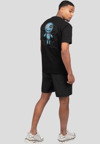 Camiseta negra de manga corta con un gráfico azul de un personaje en la parte de atrás, con una cabeza redonda y detalles cosidos.