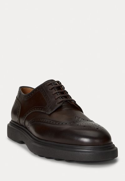 Brown leather dress shoe featuring brogue detailing, a rounded toe, and a thick black rubber sole with ridged texture. Classic lace-up design.