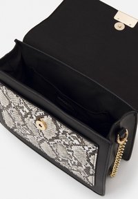 Sac à main noir avec une poche avant en cuir de serpent texturé, des détails en métal doré et une bandoulière chaîne. L'intérieur est doublé de tissu noir.