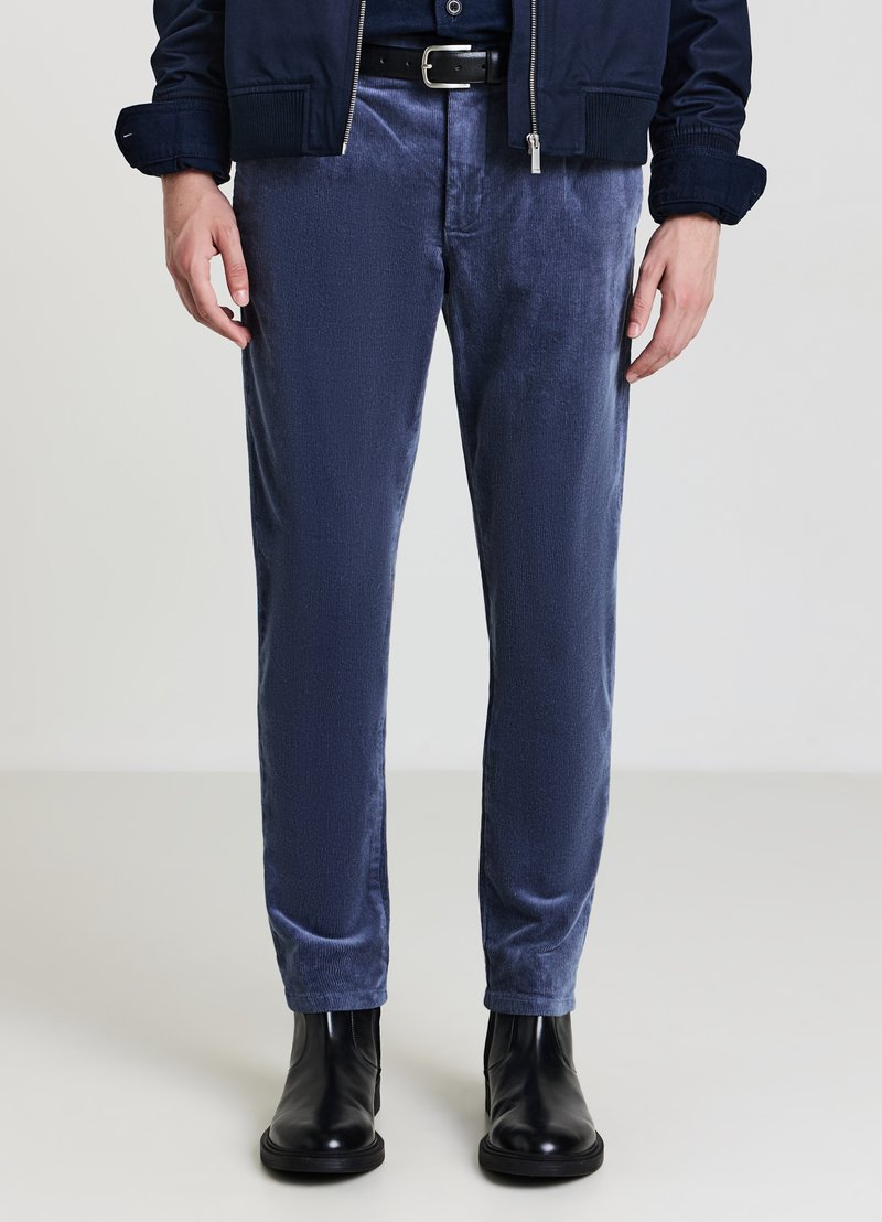Pantaloni in corduroy blu navy con superficie testurizzata, design slim fit, abbinati a stivaletti neri alla caviglia. La vita presenta una cintura nera.
