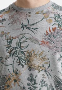 Sudadera gris claro con patrón floral en varios colores, con grandes flores naranjas y amarillas, hojas verdes y cuello redondo.