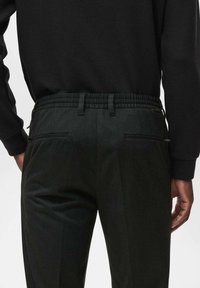 Pantaloni negri cu un finisaj texturat, prezentând un brâu elastic și buzunare laterale. Se asortează cu un top negru cu mânecă lungă.