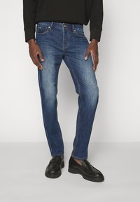 Blå jeans i denim med rak passform, femficksdesign, subtila blekningar och klassisk knappstängning. Bärs med svarta loafers.