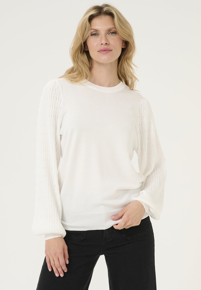 Pull en tricot blanc avec des manches bouffantes texturées, encolure ras du cou et poignets côtelés, associé à un pantalon noir ajusté. Design propre et doux.