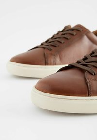 Bruine leren sneakers met een gladde textuur, ronde neuzen, bruine veters en witte rubberen zolen met een gestructureerd ontwerp.