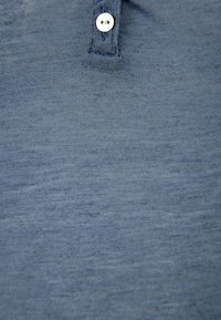 Blauwe poloshirt van zachte stof, met een gestructureerd oppervlak en een enkele witte knop bij de kraag.