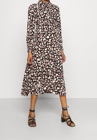 Lång leopardmönstrad klänning i mörkbrunt med rosa och krämfärgade fläckar; den har krage, långa ärmar och en svängande, lager-på-lager kjol.