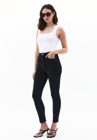 Hoge zwarte skinny jeans in denim met een gladde textuur, gecombineerd met een witte, aangesloten tanktop en zwarte, gespje haksandalen.