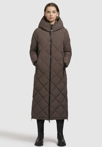 Brun quilted lang frakke med høj krave, frontlynlås, sidelommer og sorte accenter. Har hætte og en lige silhuet.