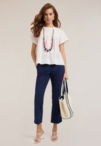 Blusa blanca de manga corta con canesú texturizado, combinada con pantalones recortados azul marino, sandalias blancas y un collar de cuentas en rojo y azul.