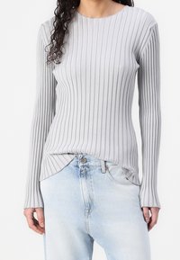 Top de manga larga de color gris claro con cuello redondo, que presenta una textura sutil y un dobladillo curvado, combinado con jeans de denim azul claro.