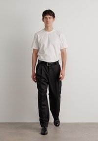 White short-sleeve t-shirt paired with black pleated trousers and black shoes. Simple design, solid colors, minimalistic aesthetic.